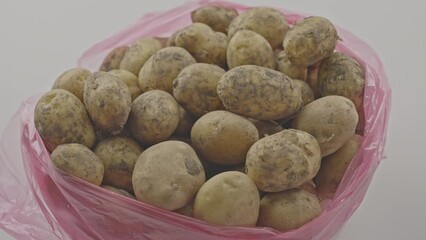 Wall Mural - Pile of unpeeled organic potatoes in pink plastic bag on white table at home. Preparation of ingredients for healthy vegetable soup