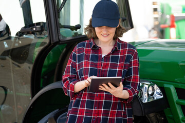 Woman farmer with a digital tablet on the background of an agricultural tractor.