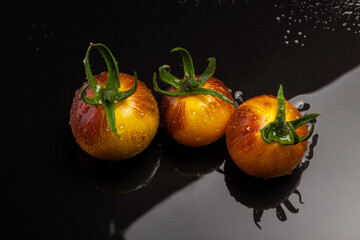 Wall Mural - Wet yellow red striped tomatoes on black wet background with water drops