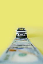 Toy Car Moving On A US Paper Currency Road On Yellow Background.