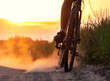 Cyclist kicks up a lot of dust from the rear wheel on a sandy road in a field at sunset.