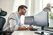 © Friends Stock - Confident businessman. Young bearded trader in formal wear is analyzing trading charts on computer screens while sitting in his modern office