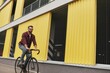 © Friends Stock - Free time. Handsome man with stubble in casual clothes riding on his bicycle along a road against yellow building