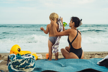 mom and son are relaxing on the beach sitting in front of the sea on a mat on a sunny summer day