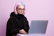 Fictional young person with dyed hair using a laptop isolated on a pink background. Generative AI.