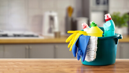 bucket with cleaning items on wooden table and blurry modern kitchen background. washing set colorfu