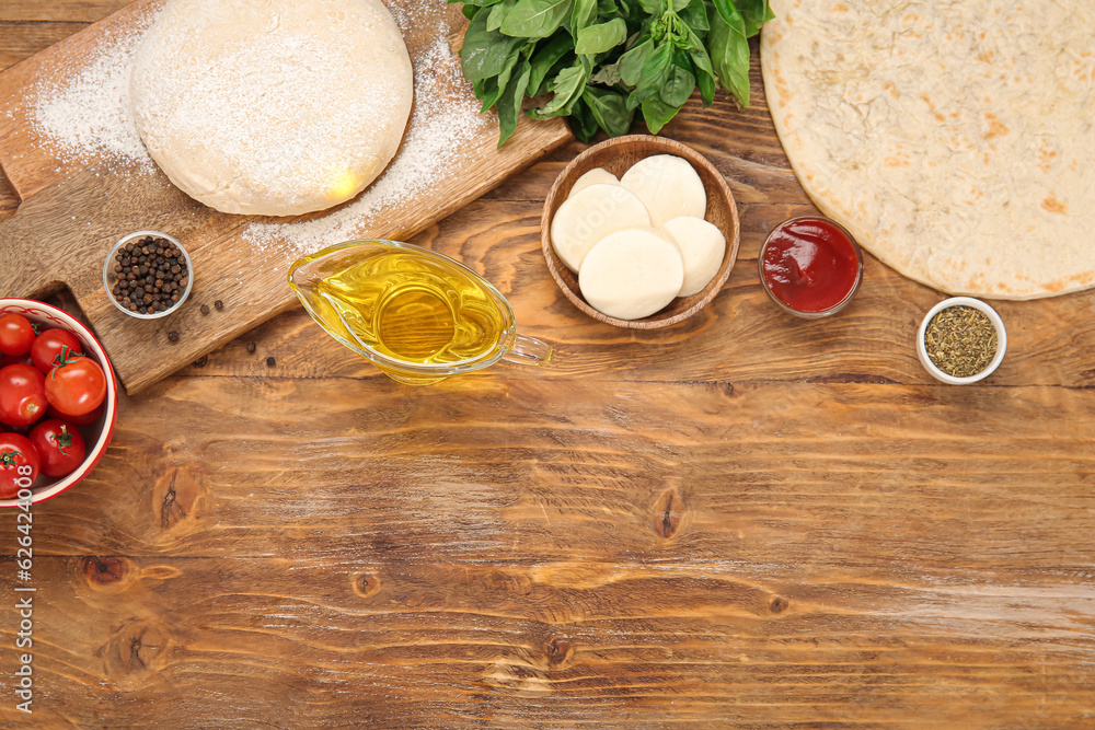 Raw dough, crust and ingredients for preparing pizza on wooden background