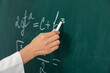 Female teacher writing Math formula on chalkboard in classroom, closeup