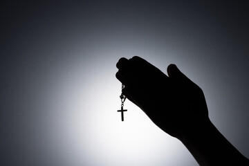 Praying hands holding a rosary, Close up holding necklace with cross, pray for god in the dark, religious Christian symbol with copy space background. God and Spiritual Concepts.