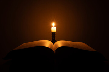 candle with bible on a old oak wooden table. beautiful gold background. religion concept.