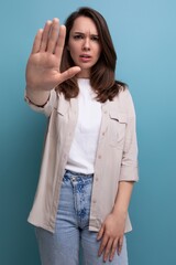 Wall Mural - suspicious caucasian young brunette woman in a shirt and jeans asks to stop on a blue background