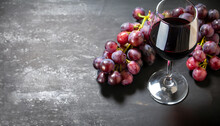 Glass Of Dry Red Wine With Bunch Of Purple Grapes On Dark Stone Table