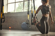© Friends Stock - Young athletic woman in sports clothing adjusting trx fitness straps while training in the gym.