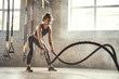 Preparing for the competition. Young athletic woman with perfect body doing crossfit exercises with a rope in the gym.