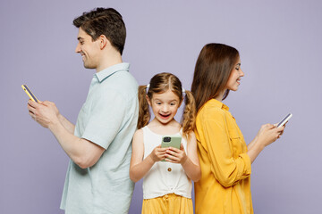 Wall Mural - Side profile view young happy parents mom dad with child kid daughter girl 6 year old wear blue yellow casual clothes hold use mobile cell phone isolated on plain purple background Family day concept