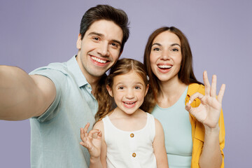 Sticker - Close up young fun happy parents mom dad with child kid daughter girl 6 year old wear blue yellow casual clothes do selfie shot pov mobile cell phone show ok okay isolated on plain purple background.