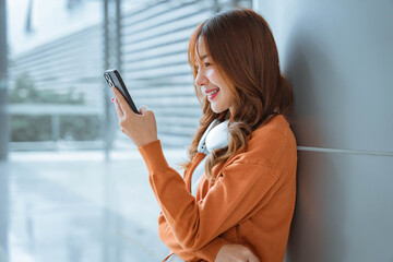 happy young asian woman holding mobile phone enjoying music listening through wireless headphones.