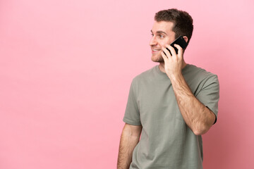 Wall Mural - Young caucasian man isolated on pink background keeping a conversation with the mobile phone