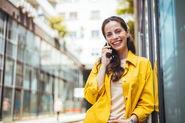 Woman walking on the sidewalk at urban setting and talking on the phone, with copy space. Portrait of attractive young woman laughing and talking on mobile phone