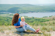 © KseniaJoyg - A mother holds a toddler child on top of a mountain with a beautiful view of the mountains and the Volga River, Russia