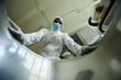 Low angle shot of black man wearing protective suit looking in tank with chemicals at pharmaceutical factory