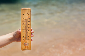 thermometer in hand on a beach background showing high temperature. hot weather and climate concept