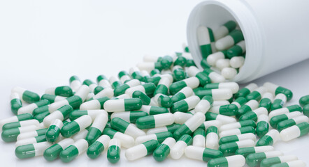 Poster - Green and white capsule pills spilled out of a white plastic bottle. Pharmaceutical industry. Prescription drug. Healthcare and medicine. Pharmacy product. Pharmaceutics. Capsule pill manufacture.