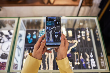 Top view closeup of unrecognizable young woman holding smartphone and taking photos or videos of jewelry display for social media, copy space