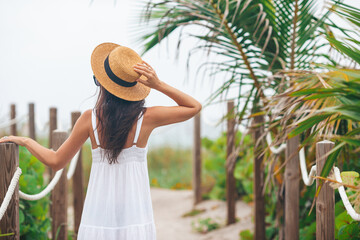 Happy woman on her way on the beach. woman in white beach dress and straw hat on summer tropical vacation