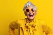 © iridescentstreet - Happy senior woman in colorful yellow outfit, cool sunglasses, laughing and having fun in fashion studio