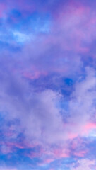 Cloudscape up view. Blue sky with pink and purple cumulus clouds in the evening at sunset. Vertical cloudy wallpaper. Natural background for design. Magic beauty in nature. Copy space. Morning colors