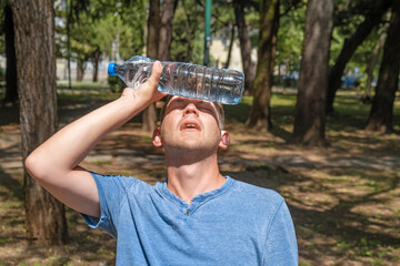 Man suffering from heat, guy with heatstroke. Caucasian male presses bottle of water to face to cool off suffering from heat wave, stuffiness