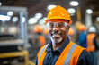 © MVProductions - Portrait of a happy African American factory worker wearing hard hat and work clothes standing besides the production line