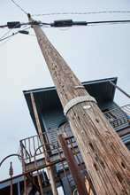 Tall Telephone Pole Bottom Up View With Rusty Metal Railing On Blue House In Background