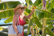 © weyo - A woman in a retro swimsuit and with a beach bag near a banana tree in a tropical resort.