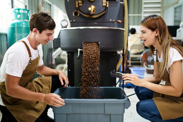 Professional male and female coffee roasters working with modern automated roasting machine in the coffee roasting factory. Coffee roasters checking or inspecting the roasting quality of coffee bean.