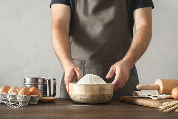 Poster - Male baker with ingredients for making dough on wooden table in a bakery