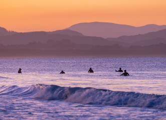 Wall Mural - Sunset view of surfers in silhouette along the Belongil Beach area in Byron Bay, New South Wales, Australia
