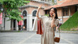 A happy Asian woman with her shopping bags is talking on the phone with her friend on the street.