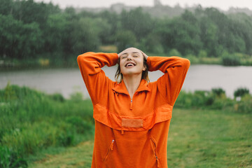 Portrait of a young girl in an orange sweater enjoying the rain on a summer day. The girl is having fun and dancing under the summer rain