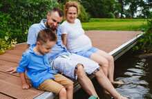 Family Spending Leisure Time With Family Sitting On Footbridge Over Lake