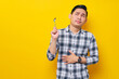 © Bangun Stock Photo - Hungry young Asian man wearing white checkered shirt holding a spoon and thinking of delicious food to eat isolated on yellow background. People Lifestyle Concept