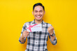 © Bangun Stock Photo - Excited young Asian man wearing a white checkered shirt holding a gift voucher and celebrating the winner isolated on yellow background. People Lifestyle Concept