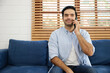 © offsuperphoto - young handsome man sitting on sofa and talking by smartphone at home