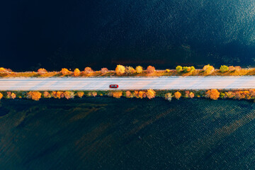 aerial view of fall road and blue water lake sea ocean. red car with a roof rack on a country road i