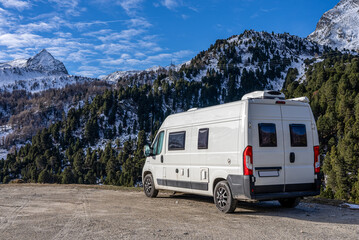 6m long white camper van in the mountains. The Camper is parked in an unpaved square and you can see the left side. The VanLife in the mountains in Switzerland.