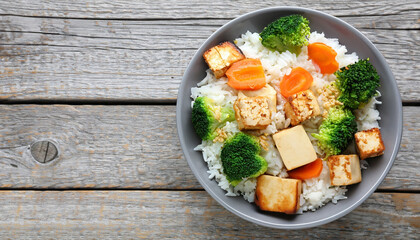 Wall Mural - Bowl of rice with fried tofu, broccoli and carrots on grey wooden table, top view
