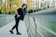 Active Brunette In Casual T-shirt And Leggings Holds Dumbbells, Poses At A Bridge, Goes For Outdoor Sports. Leading A Healthy Lifestyle, Lifting Weights, Using Sports Equipment.