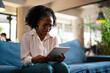 © JustLife - Beautiful African businesswoman sitting on sofa in office. Young tired woman using digital tablet.