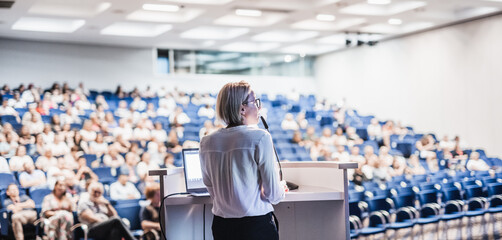 Wall Mural - Female speaker giving a talk on corporate business conference. Unrecognizable people in audience at conference hall. Business and Entrepreneurship event